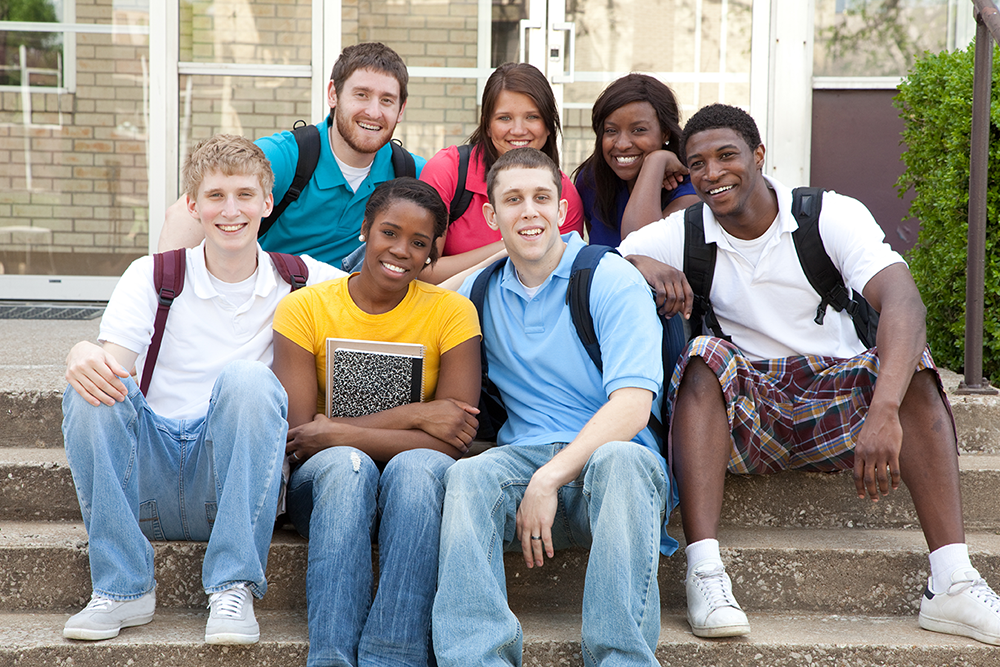 Students sitting on the steps of a building on a campus.