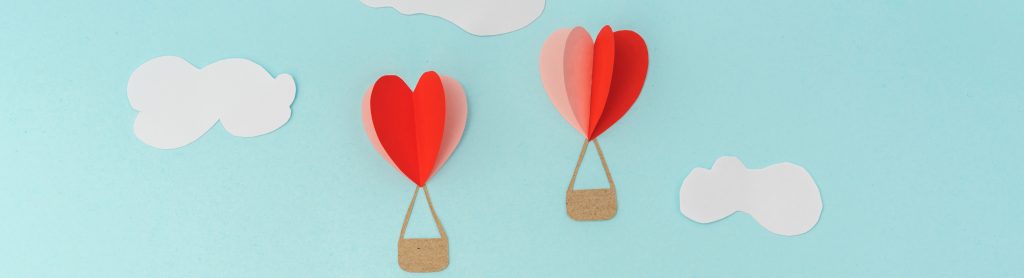 Graphic with two hot air balloons shaped like hearts floating in the clouds.