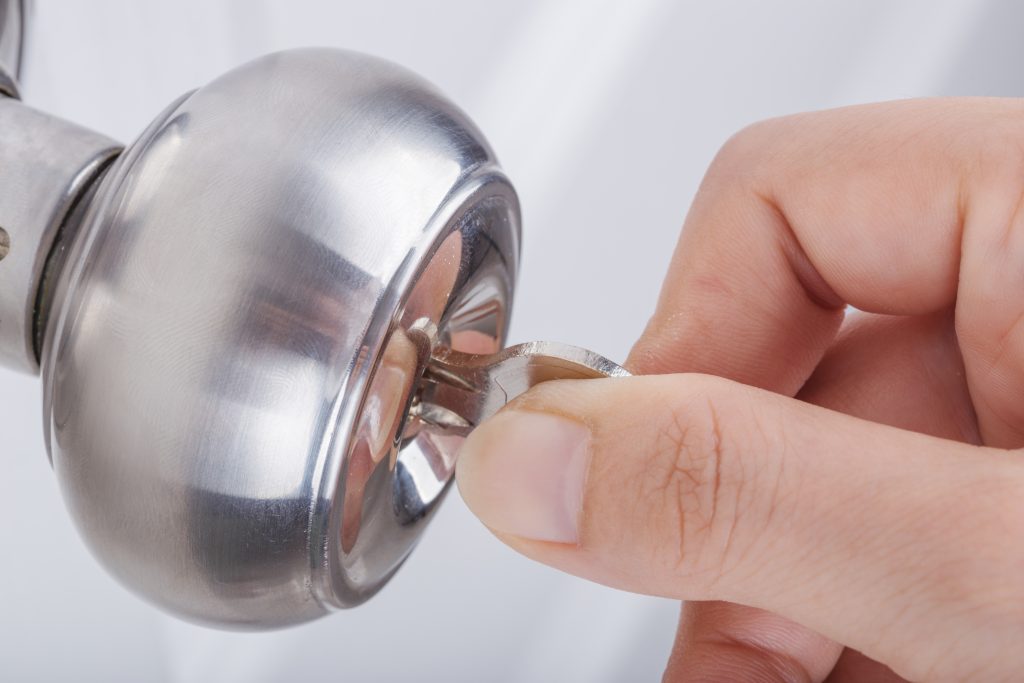 A hand holding a key, inserting it into a door knob key slot